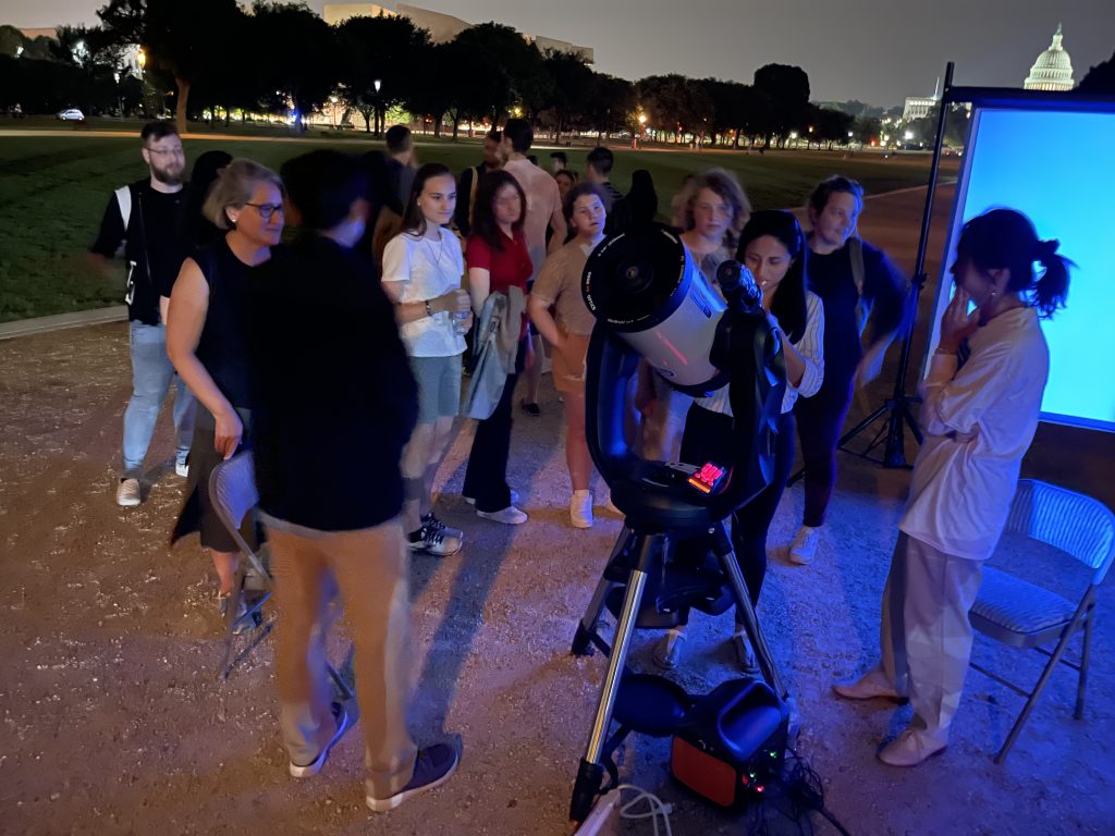 A crowd observing the night sky through telescopes on the National Mall