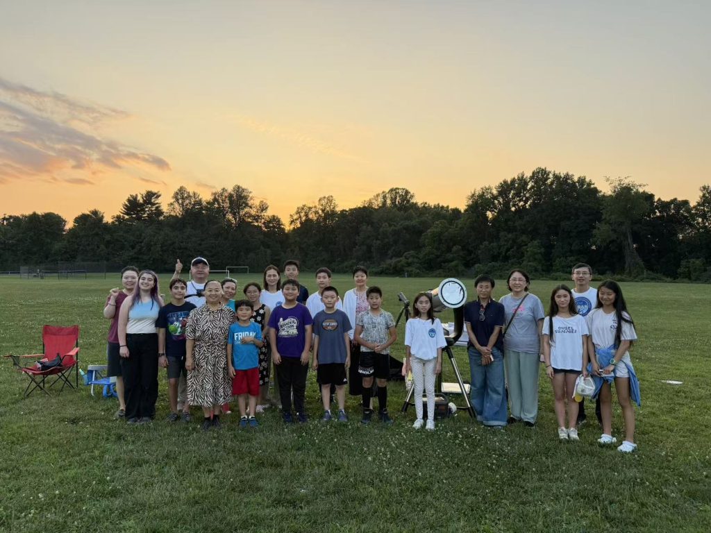 Participants and a telescope on a school lawn at sunset