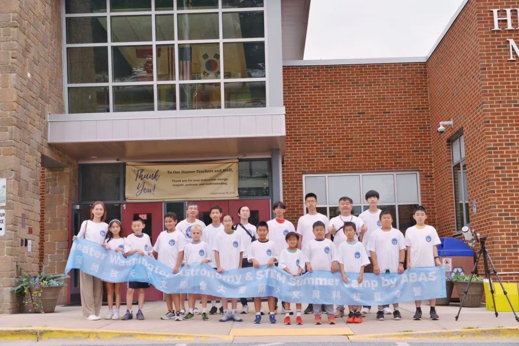 Campers and instructors holding an ABAS summer camp banner outside the school