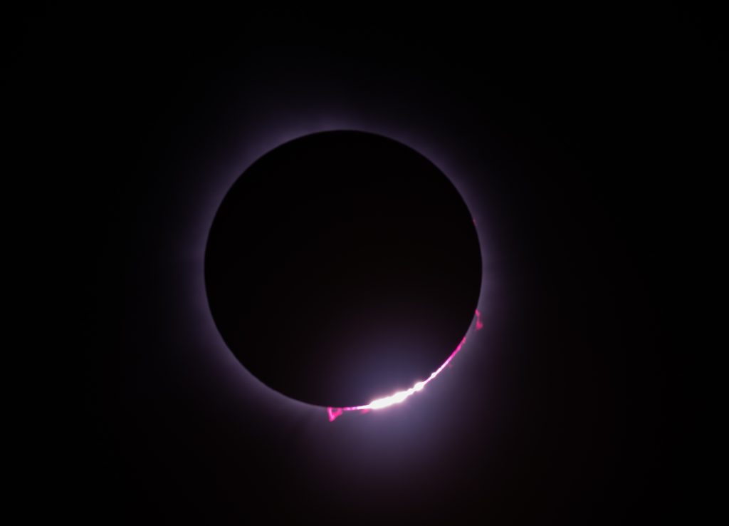 Close-up of the eclipse near totality, with bright points along the Moon’s edge and red prominences