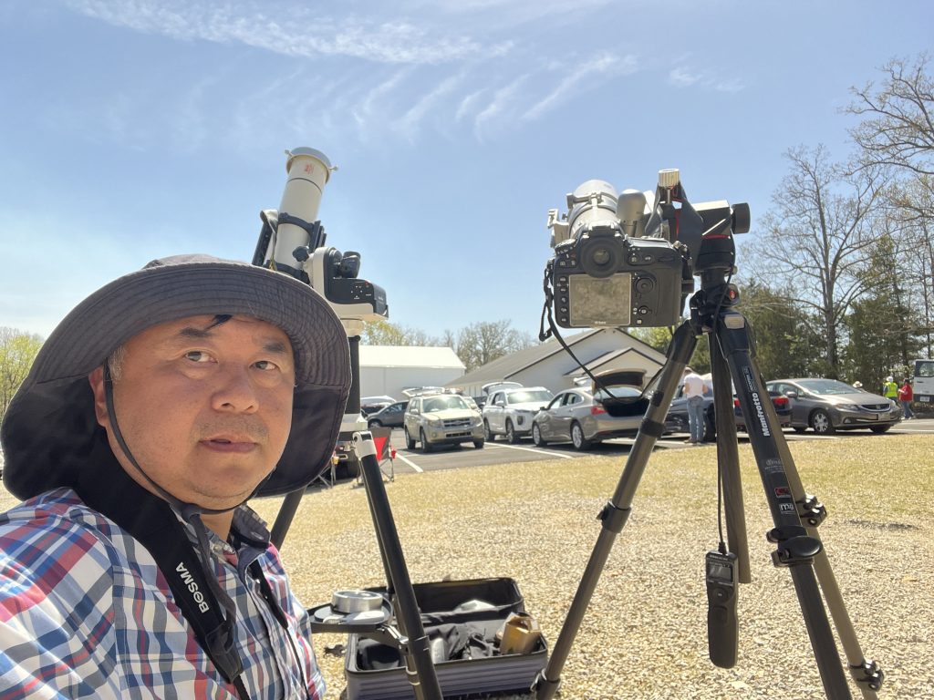 Renjiang Xie beside two telescope-and-camera setups pointed at the Sun in Ozark Acres, Arkansas