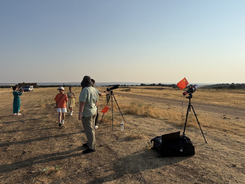 Telescopes, cameras, and tripods set up on high ground in Lerma, with a computer and equipment bags on the grass