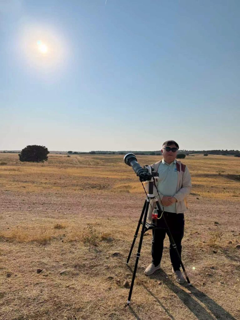 A team member beside a telescope with a camera attached at the rear, mounted on a tripod