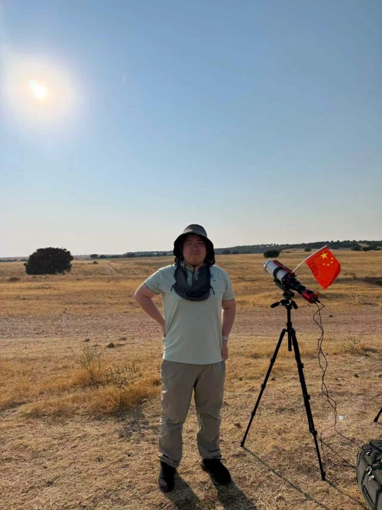 A team member beside a telescope with a red imaging camera and a flag planted next to it