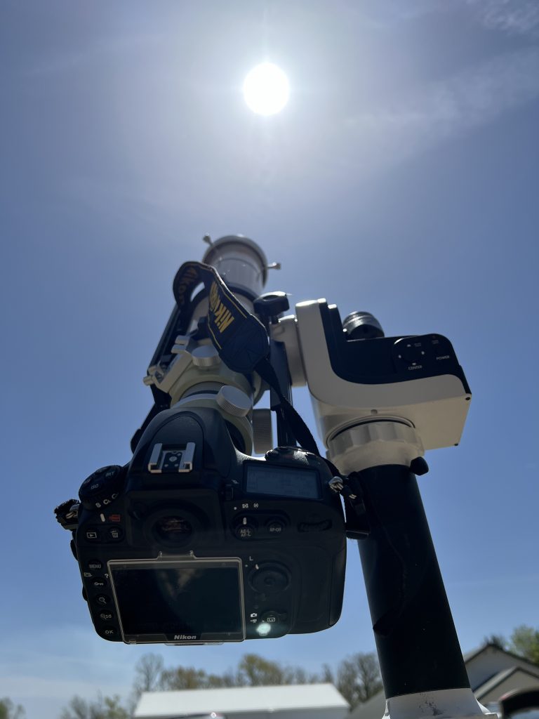 A camera attached to the rear of a telescope on a white mount, pointed at the Sun